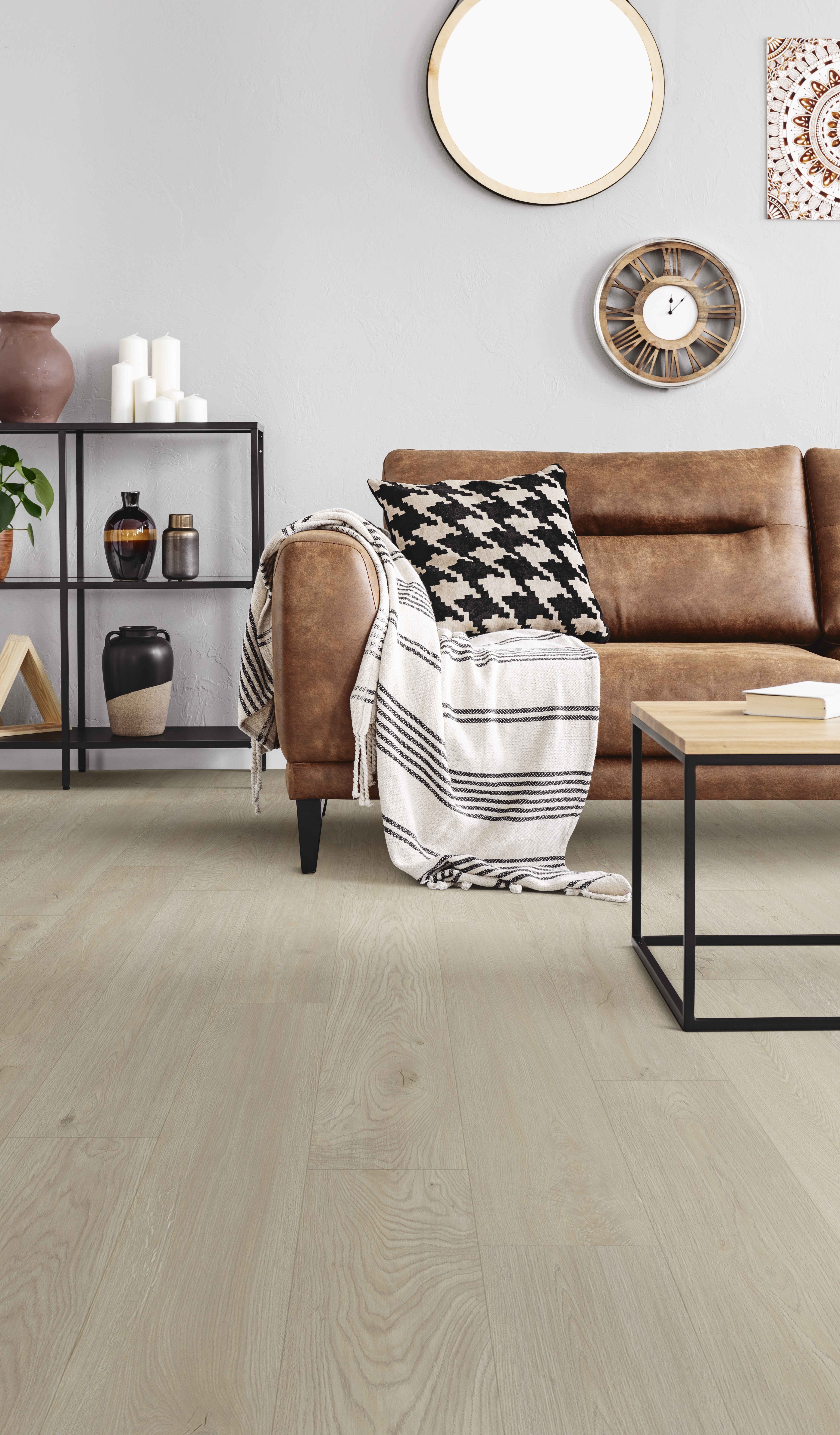 Vertical view of warm ethno living room with leather couch with patterned pillow and mirror and clock on beige wall, real photo