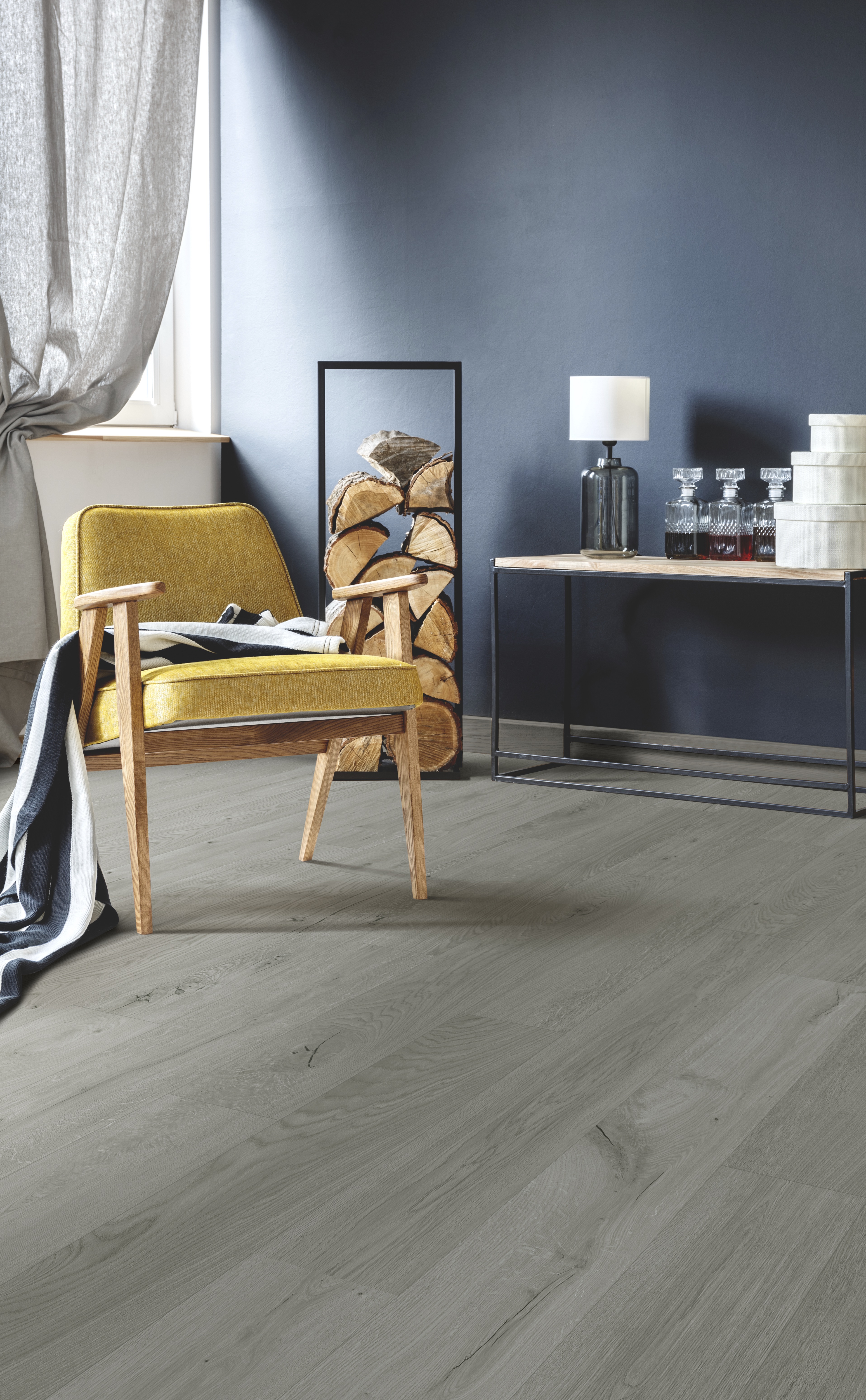 Wooden yellow armchair with blanket standing on white rug in stylish living room with wood logs, black wall and gray curtains