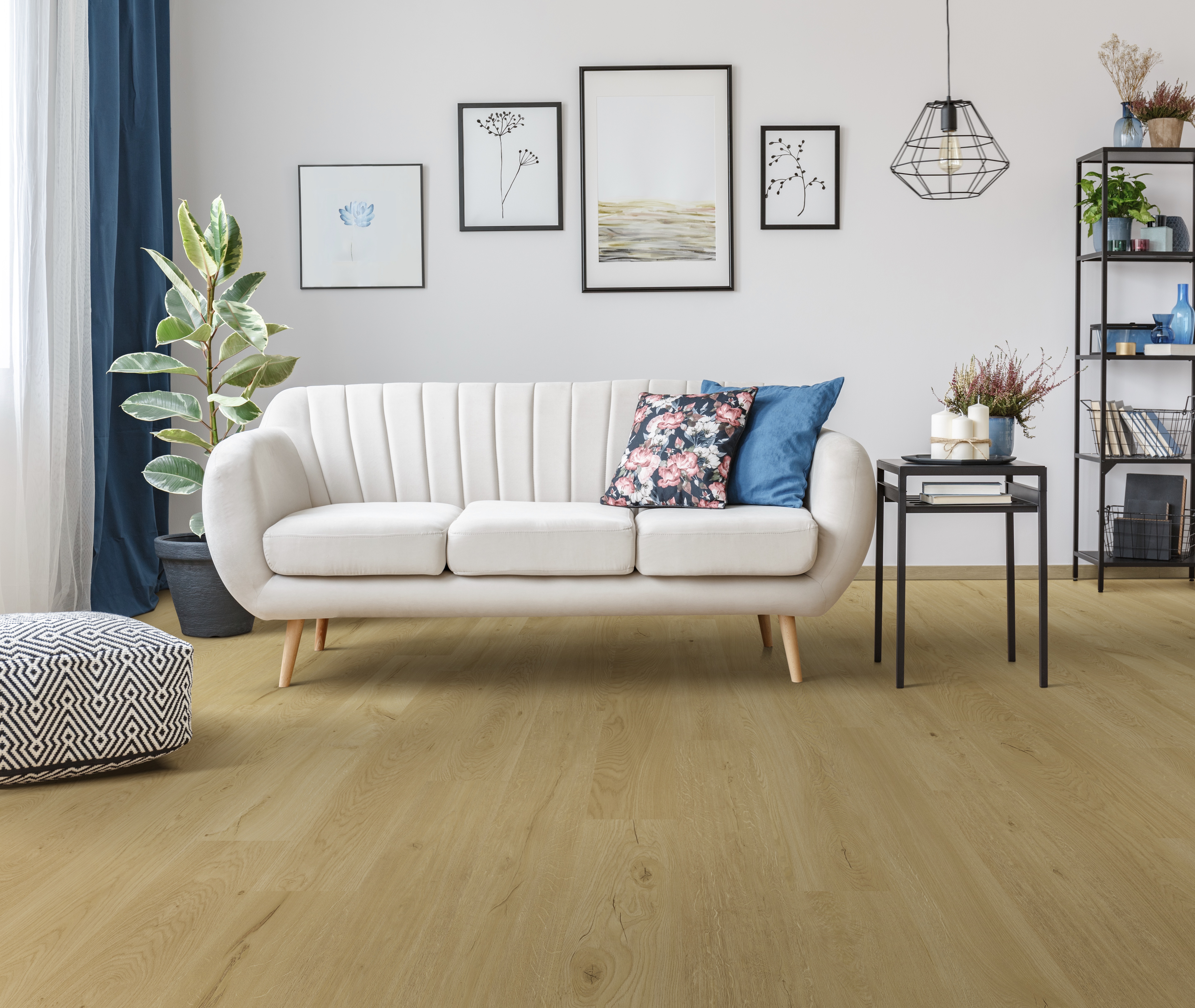 Floral pillow on beige sofa next to table with candles in living room interior with pouf and posters
