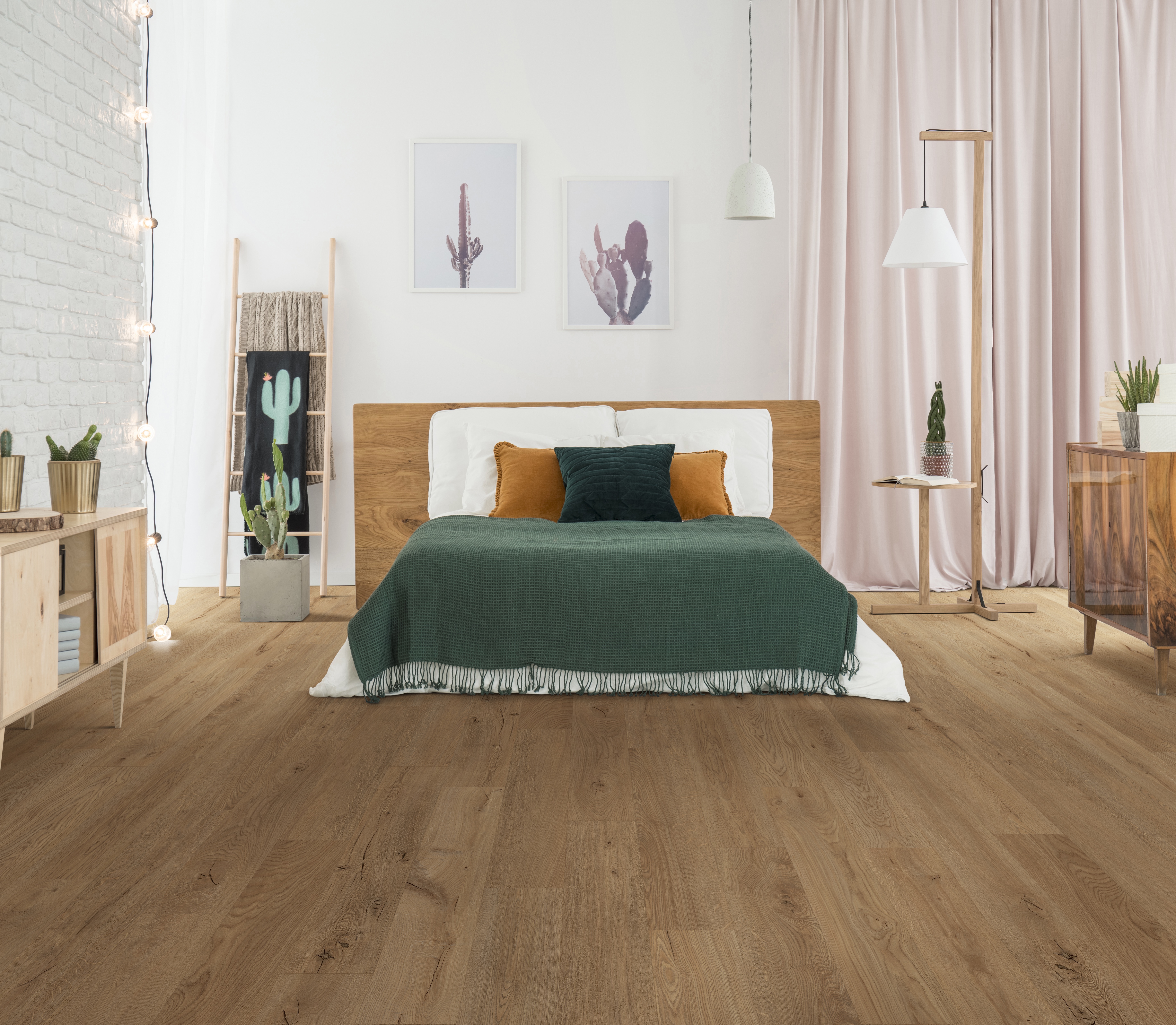 Dark blanket and pillows on king-size bed in rustic bedroom interior with lamp, cacti and wooden furniture